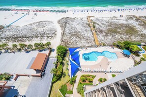 Vista aérea de un complejo turístico con piscina, sombrillas de playa y un paseo marítimo.