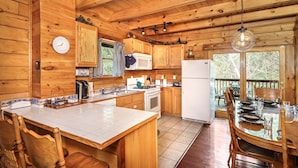 Une cuisine rustique aménagée dans une cabane en bois, avec un grand îlot central, des meubles de rangement en bois, un réfrigérateur et un coin repas comprenant une table et des chaises.