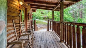 Une cabane en bois dotée d’un porche, de chaises en bois et offrant une vue sur une zone boisée.