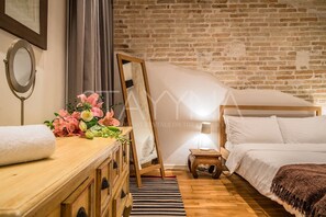 A cozy bedroom with a wooden dresser, a bed, a nightstand, and a brick wall.