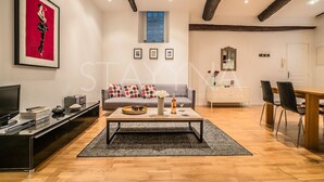 A modern living room with a sofa, coffee table, and a TV. There is a dining area with a table and chairs. - Pebble Loft 1 bedroom apartment VRBO (Nice)