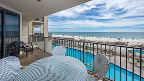 A balcony with a pool, overlooking a beach with umbrellas and people.