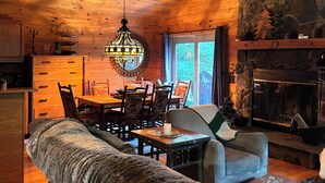 Interior acogedor de una cabaña con una mesa de comedor, sillas, un sofá, chimenea y una lámpara de araña grande.