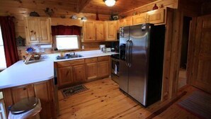 A wooden cabin kitchen with a refrigerator, wooden cabinets, a sink, and a window.