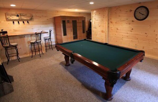 A pool table with chairs, a clock on the wall, and a bar area.
