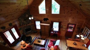 A cozy cabin interior with a fireplace, wooden walls, a stone fireplace, a bear decoration, and a large window.