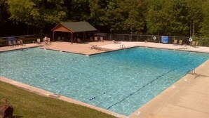 A rectangular swimming pool with clear blue water, surrounded by a deck with lounge chairs and a small pavilion.