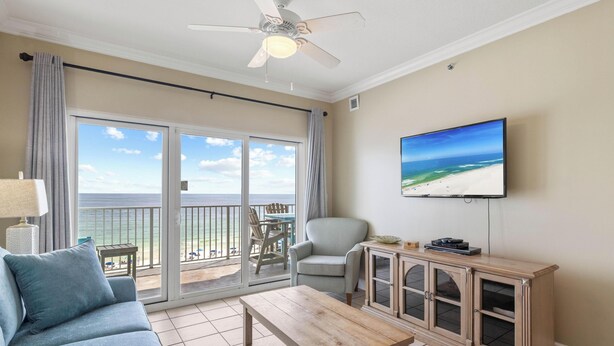 Ett rum med en soffa, ett träbord, en tv och utsikt över stranden.