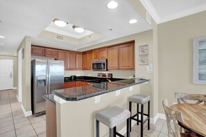 A modern kitchen with wooden cabinets, stainless steel appliances, and a granite countertop. - Seawind 608 by Liquid Life (Gulf Shores)