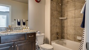 A bathroom with a marble countertop, a toilet, a shower, and a bathtub.