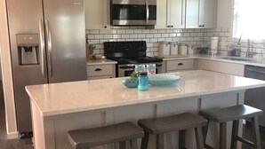 Une cuisine moderne dotée d’un grand îlot central, d’appareils électroménagers en acier inoxydable et de luminaires suspendus.