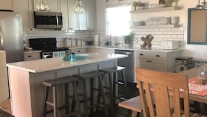 Une cuisine moderne avec des armoires blanches, des appareils en acier inoxydable et un îlot central doté de tabourets de bar.