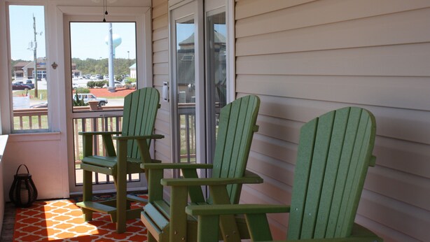 Une véranda avec des fauteuils Adirondack verts et une vue sur un parking.
