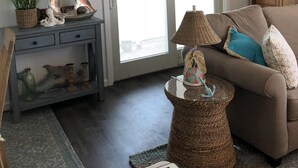Un salon chaleureux avec un parquet en bois foncé, un canapé marron, une petite table d’appoint en osier et un panneau décoratif au-dessus de la porte.