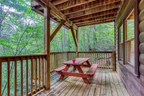 A wooden deck with a picnic table, surrounded by a wooden railing, overlooking a forested area. - Awesome Honey Bear, “Cozy Cabin Retreat in the Smokies – Comfort & Fun for All”! (Sevierville)