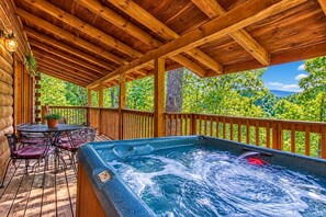 Une terrasse en bois avec un jacuzzi, des sièges d’extérieur et une vue sur un paysage boisé.