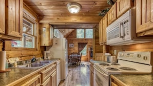 A wooden cabin kitchen with a central island, a refrigerator, a stove, and a microwave. - Awesome Honey Bear, “Cozy Cabin Retreat in the Smokies – Comfort & Fun for All”! (Sevierville)