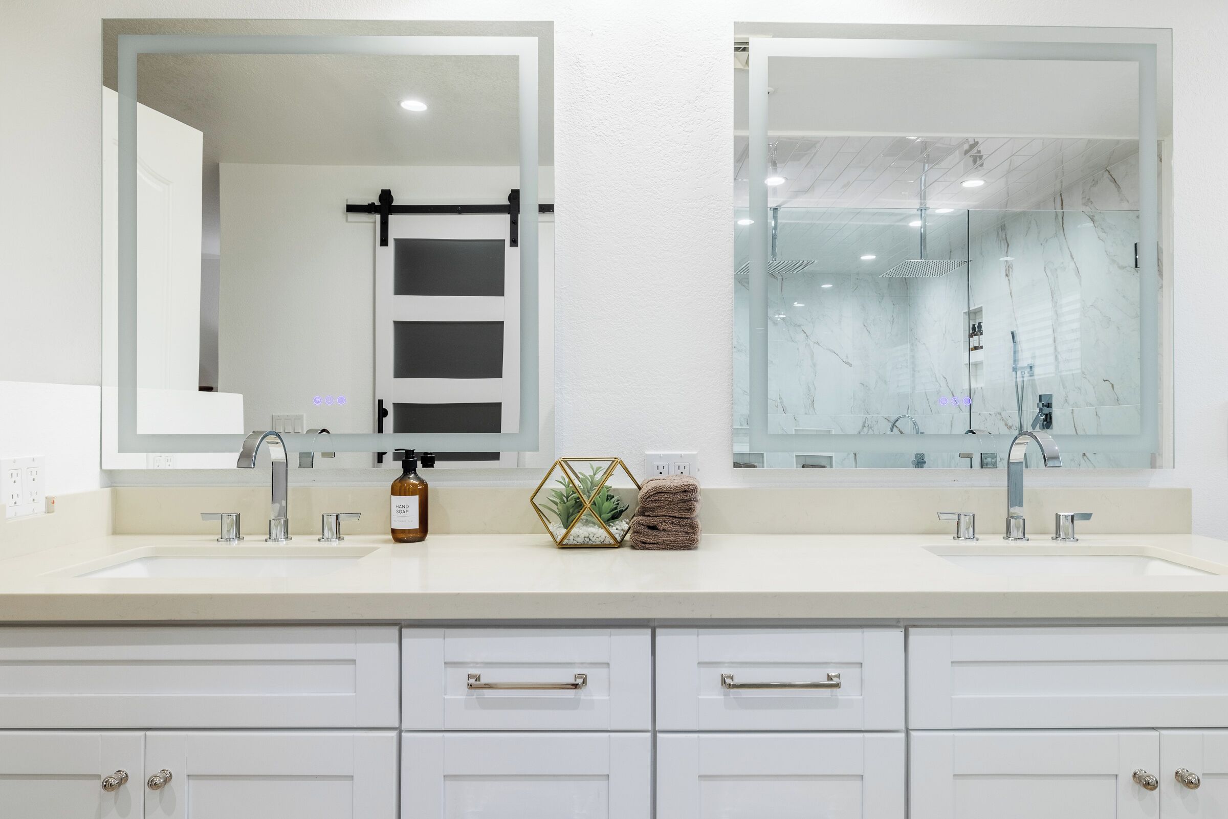 A modern bathroom with two sinks, large mirrors, and white cabinetry.