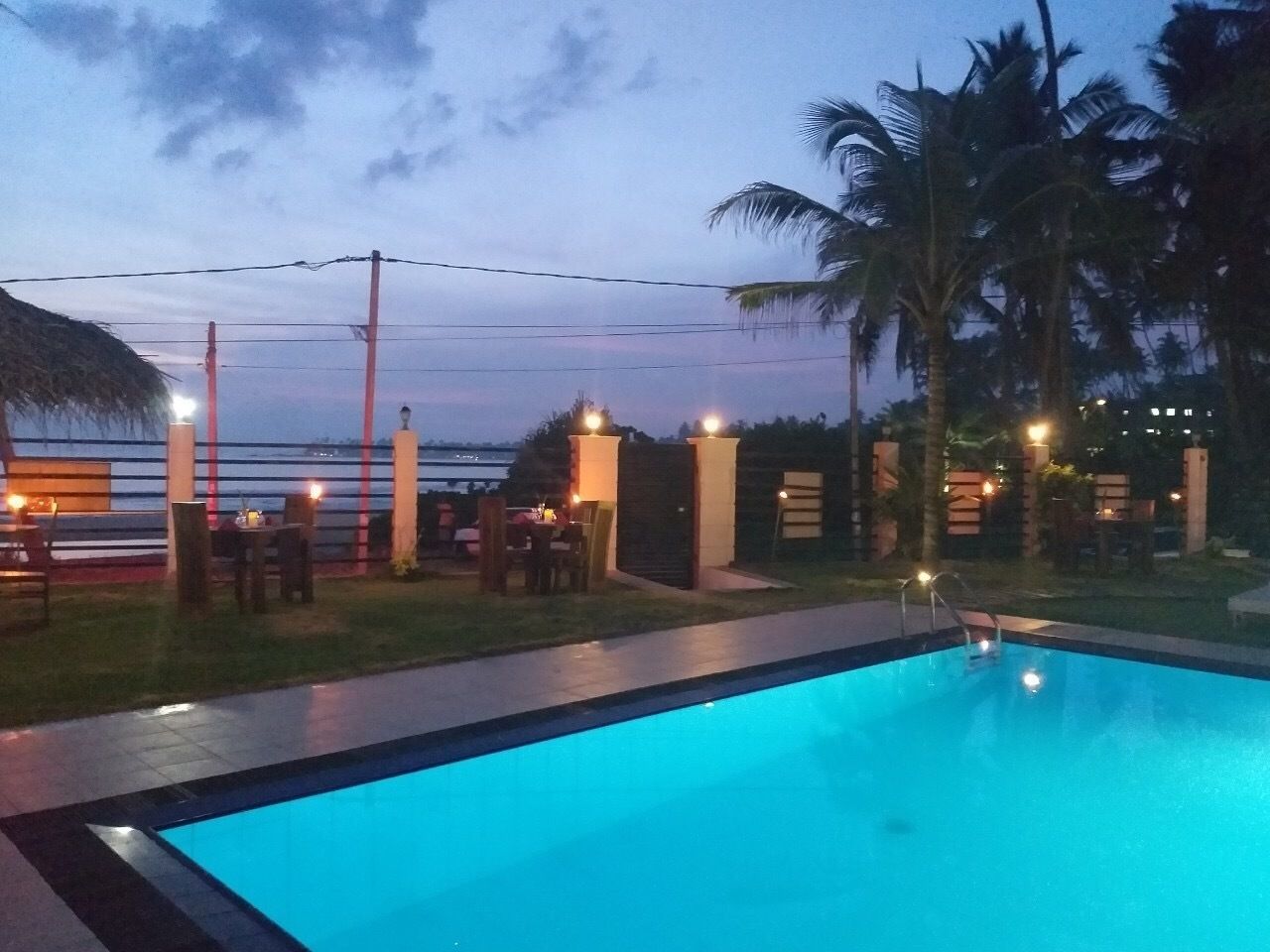 A swimming pool with a view of the sunset, palm trees, and outdoor seating area.
