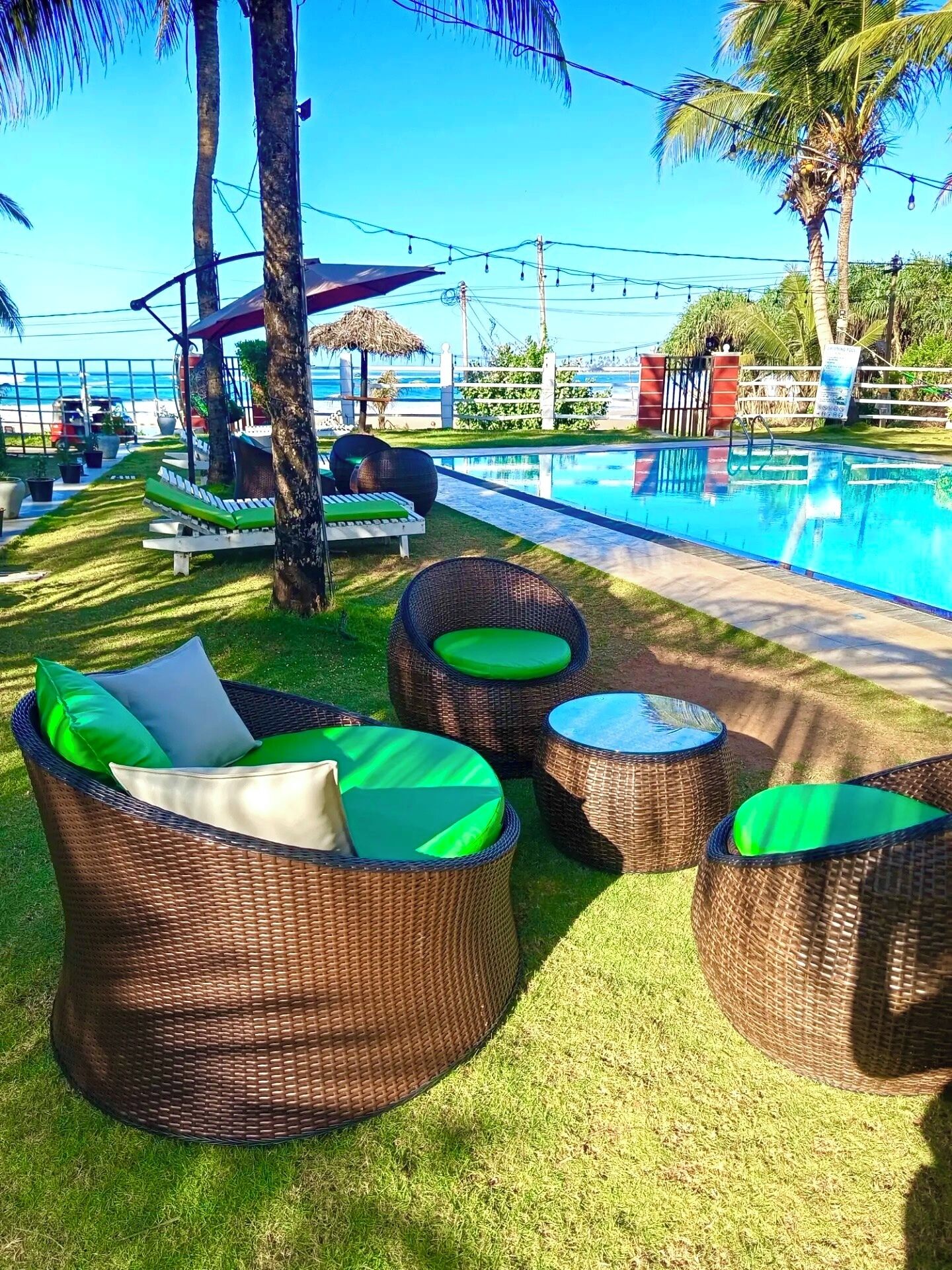 Zona junto a la piscina con mobiliario de mimbre, piscina y vista al océano.