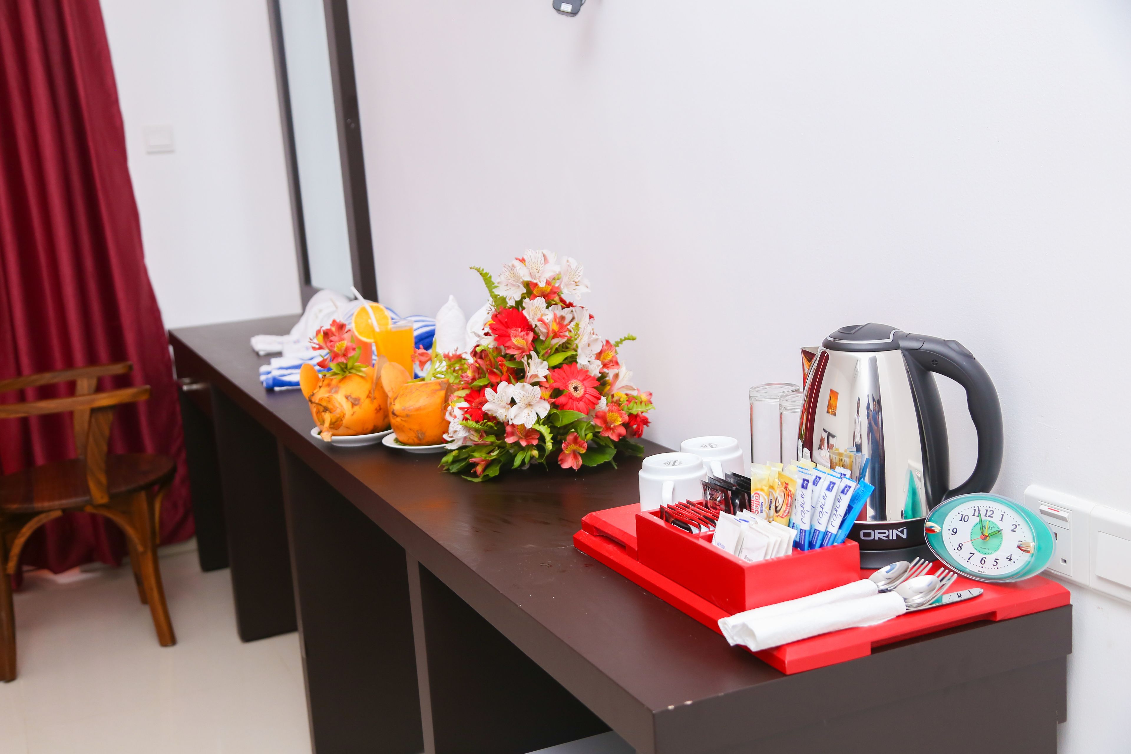 Ein Hotelzimmer mit Esstisch, gedecktem Tisch, einer Blumenvase, einem Wasserkocher, einer Uhr und verschiedenen Gewürzen.