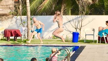 Ein Pool mit Personen, die hineinspringen, umgeben von Palmen und einer weißen Mauer.