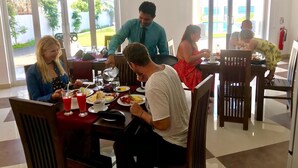 A restaurant with large windows, tables with red tablecloths, and diners. - Crystal Resort Dickwella (Dikwella)