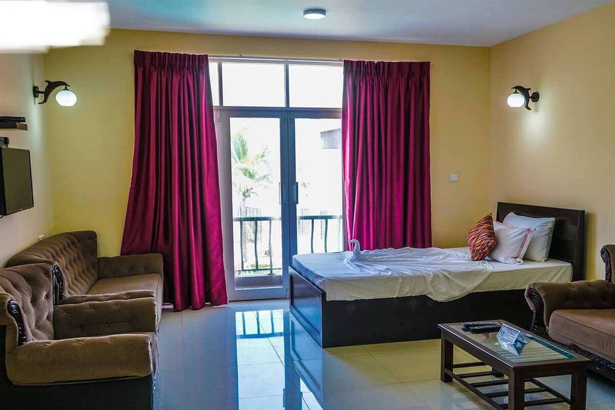 A hotel room with a bed, two sofas, a glass coffee table, and a sliding door to the outside.