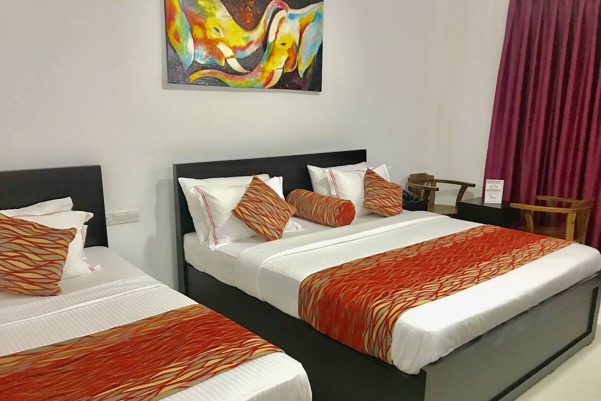 Two beds with patterned bedding, a nightstand, a chair, and a painting on the wall.