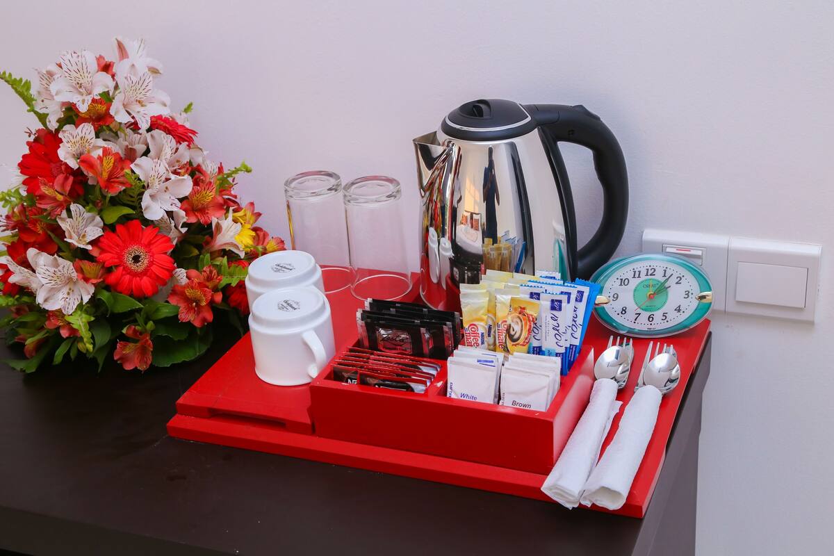 A red tray with a coffee maker, tea bags, a clock, and a vase of flowers.
