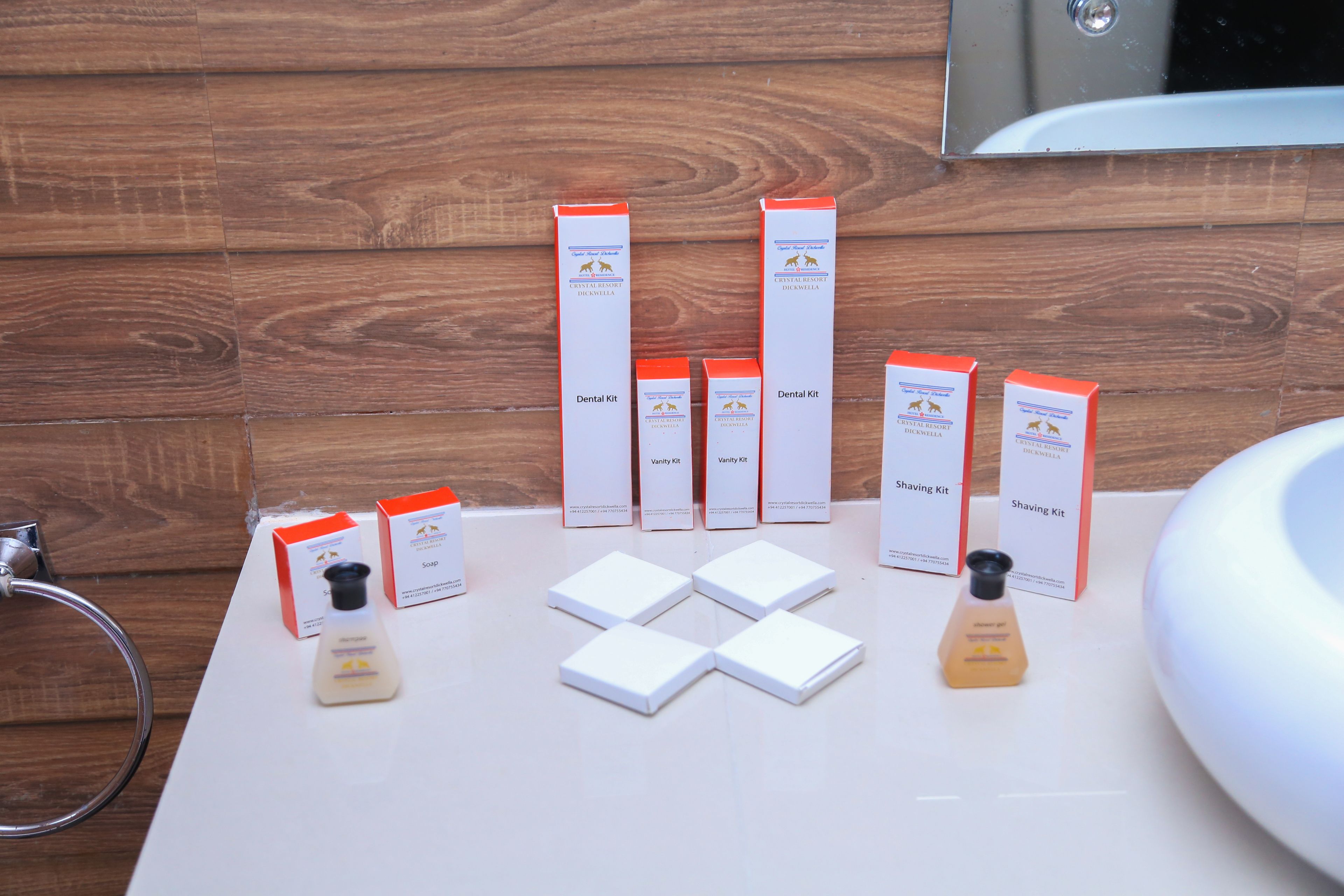 A bathroom with wooden paneling, a white sink, and multiple boxes of dental and shaving kits.