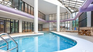 Una piscina interior con vistas despejadas del entorno, que incluye una zona de estar con mesas y sillas, y una estructura de techo de vidrio.