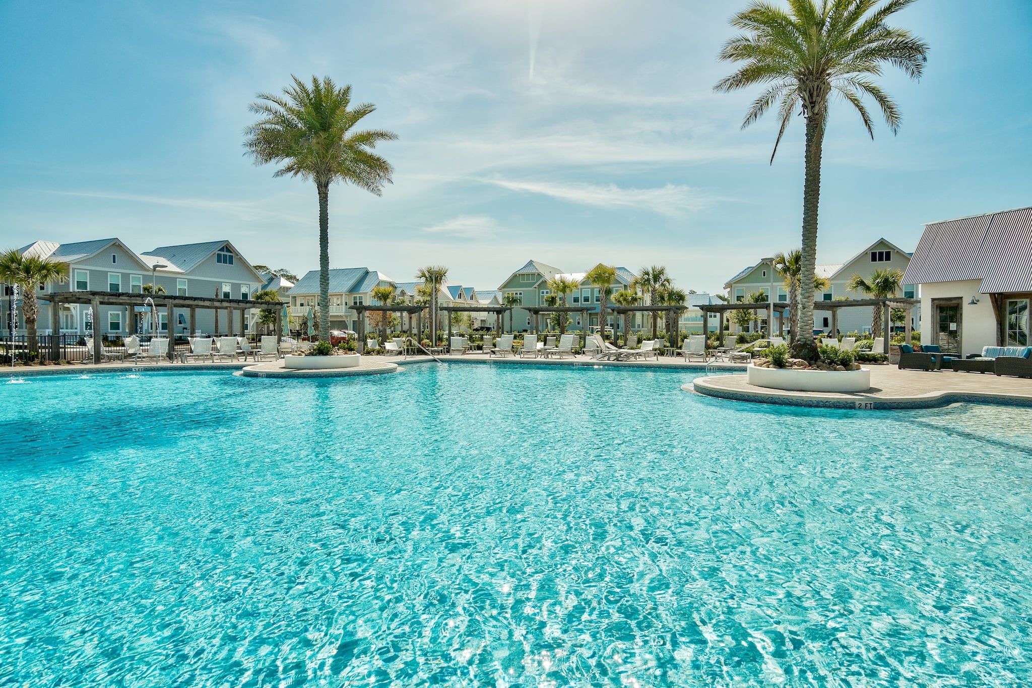 Piscina com espreguiçadeiras e palmeiras, cercada por edifícios com estilo de resort.