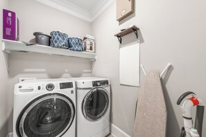 A laundry area with two front-loading washing machines, a shelf with storage items, and a hanging towel rack.