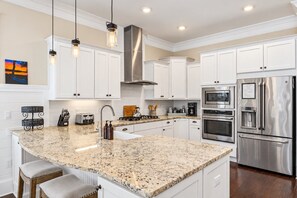 A modern kitchen with white cabinets, granite countertops, stainless steel appliances, and pendant lighting.