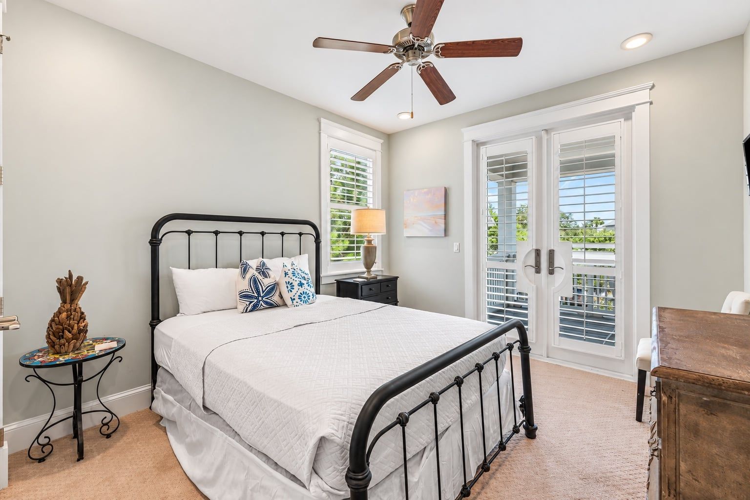 A bedroom with a bed, a nightstand, a lamp, a ceiling fan, and a view through a sliding glass door.
