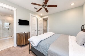 A bedroom with a bed, a ceiling fan, a TV, a wooden cabinet, and a walk-in closet.