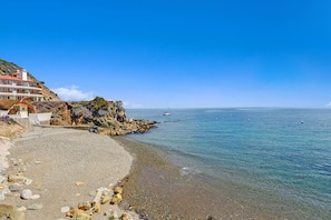 A coastal building with a rocky shoreline and clear blue sea.