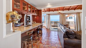 A kitchen with a bar area, wooden cabinets, and a view to the outside. - Remodeled 1B|1B Villa,Golf Cart, WIFI, Gorgeous Panoramic Ocean Views, golf cart (Avalon)