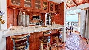 A kitchen with wooden cabinets, a marble countertop, and a view to the outside. - Remodeled 1B|1B Villa,Golf Cart, WIFI, Gorgeous Panoramic Ocean Views, golf cart (Avalon)