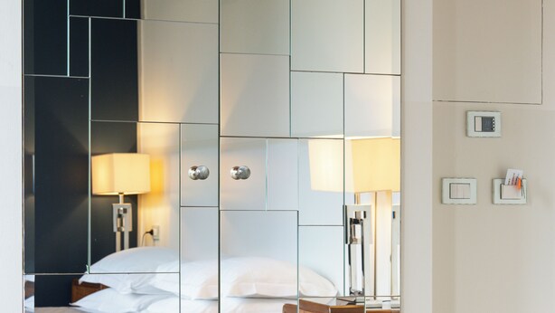 A hotel room with a mirrored wardrobe, a bed with a quilted cover, a wooden nightstand, and a lamp. - Hotel la Scala (Florence)