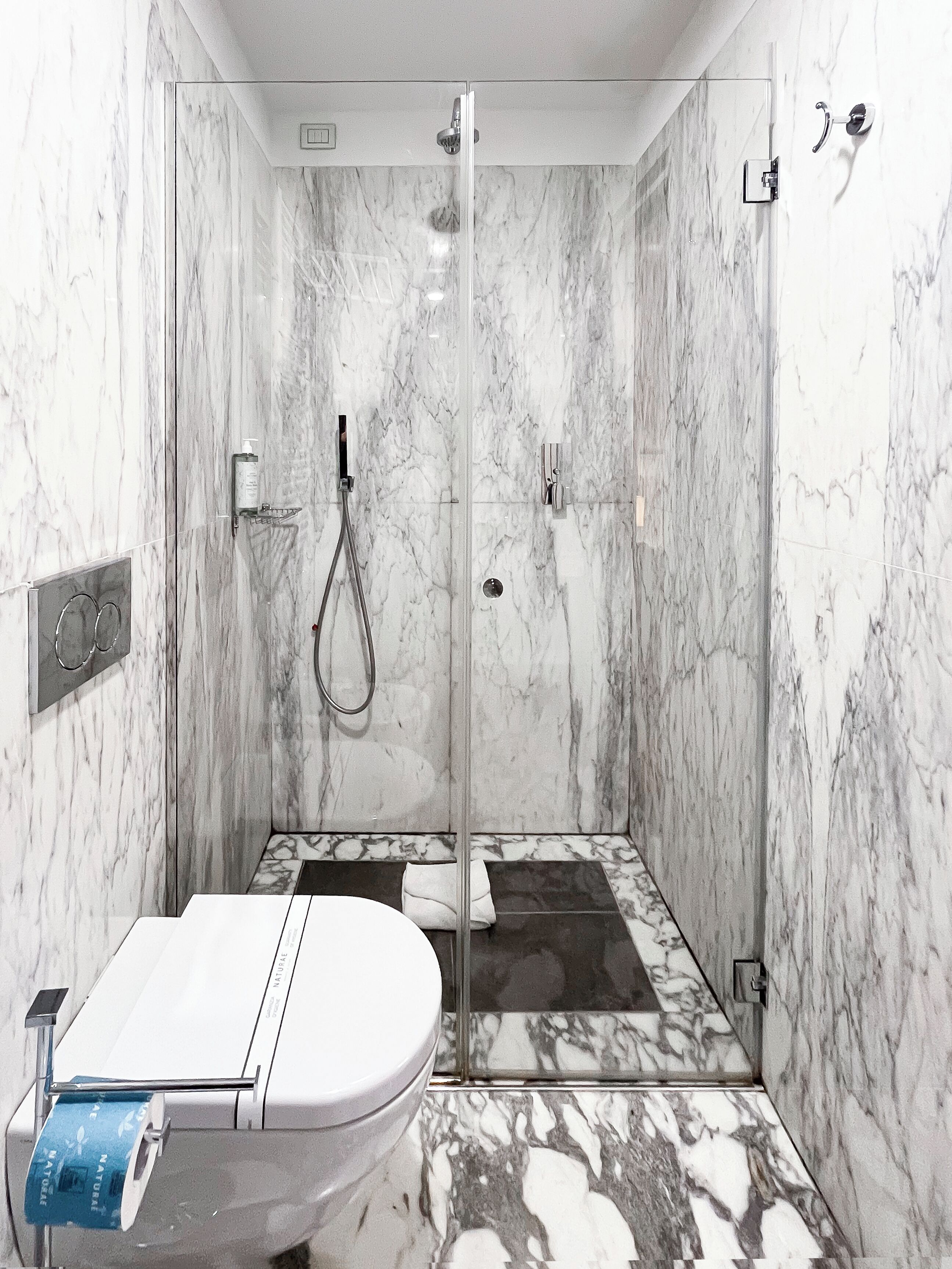 A bathroom with a marble shower, a toilet, and a bidet.