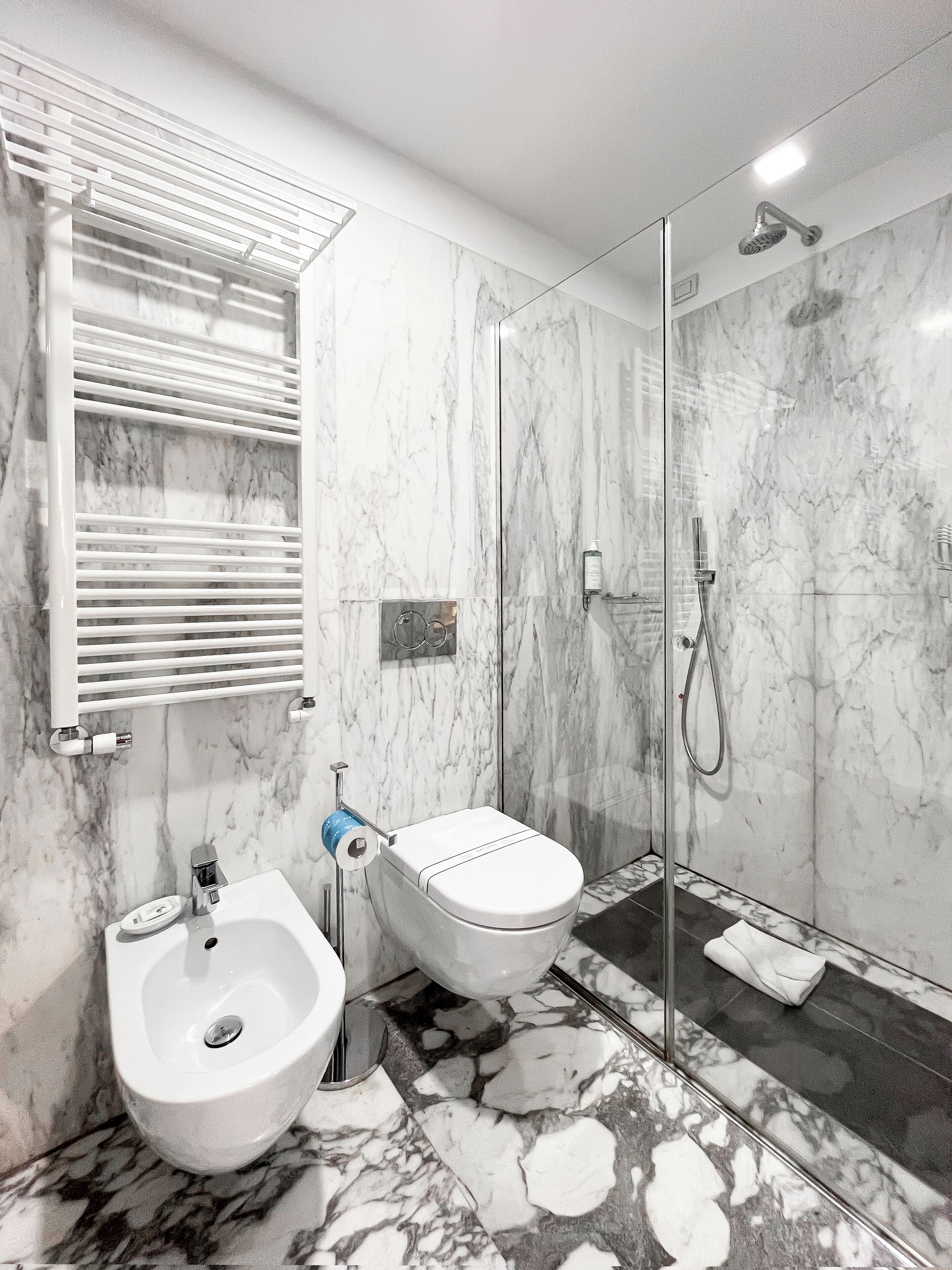 A modern bathroom with a bidet, a toilet, a shower, and marble flooring.