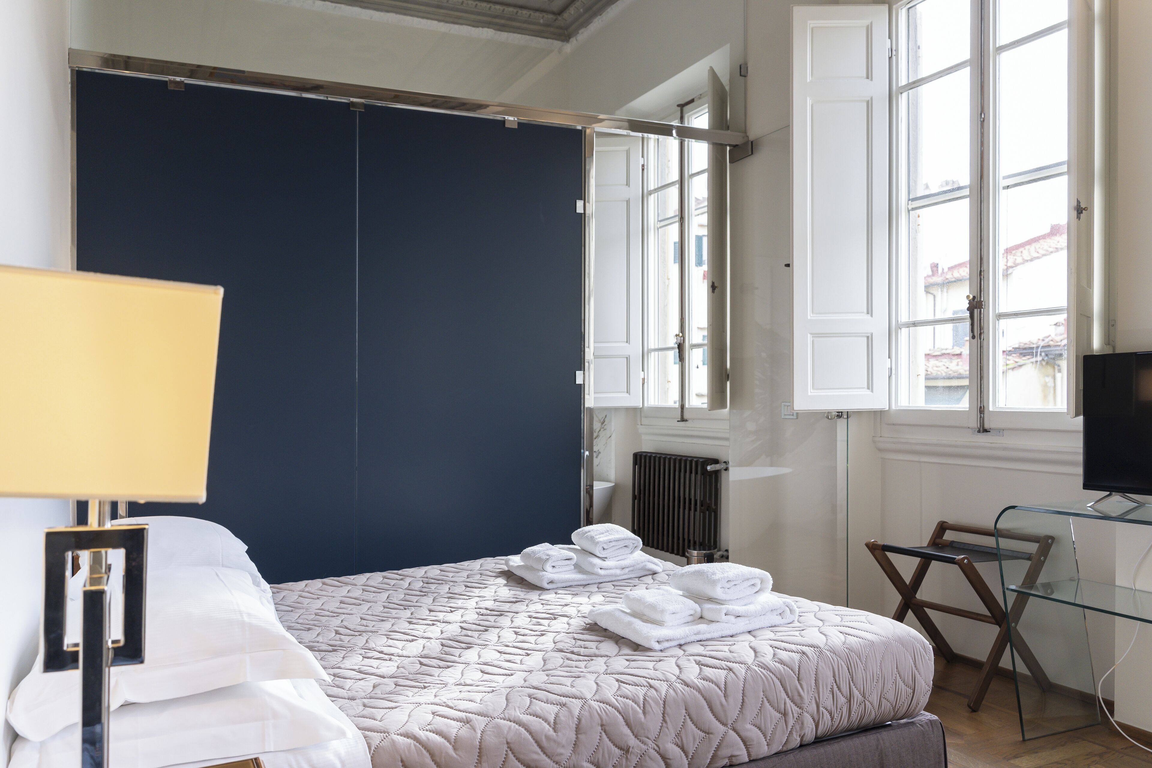 A bedroom with a large bed, a desk, a chair, and a window with curtains.