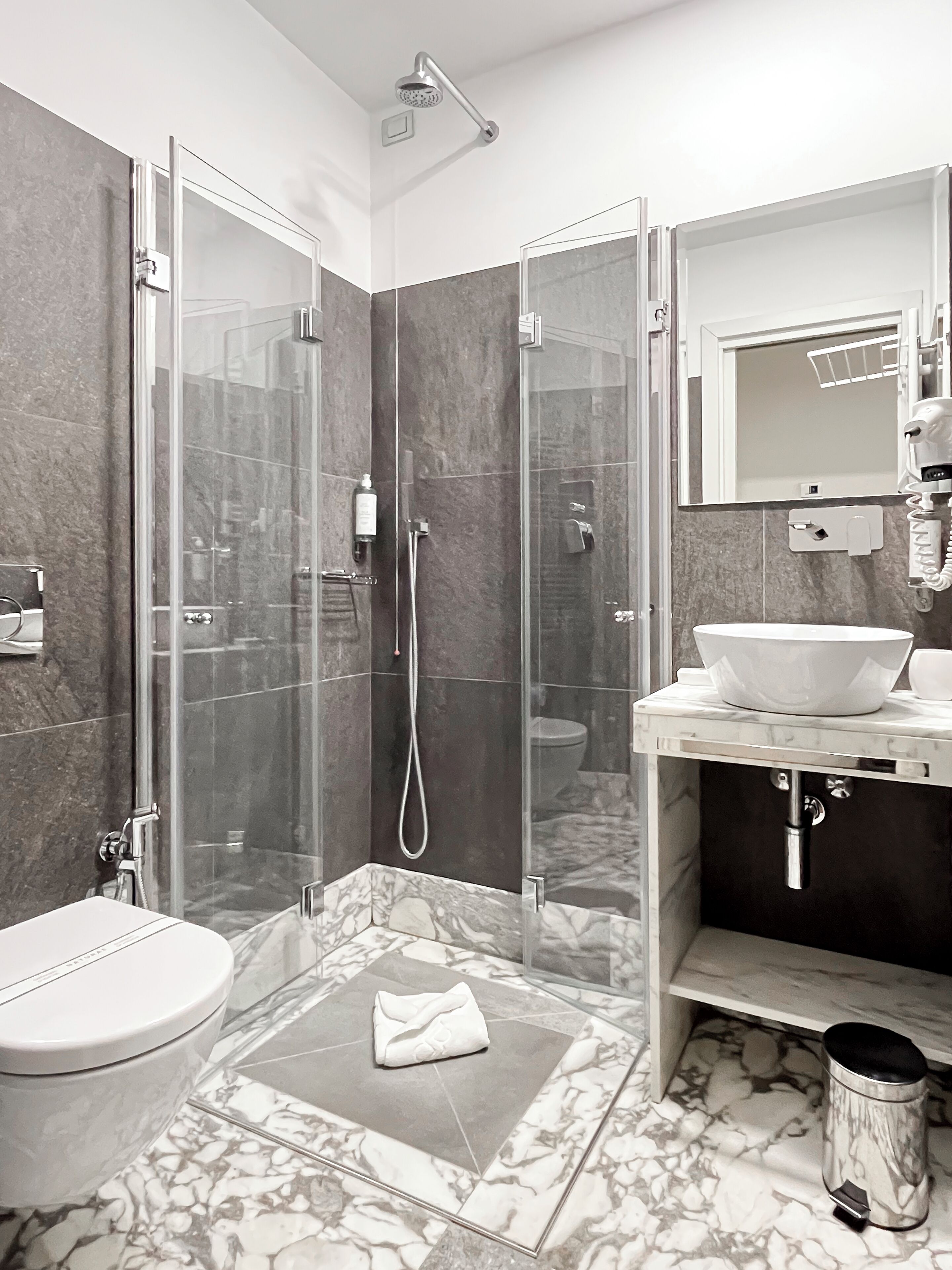 A modern bathroom with a glass-enclosed shower, a white sink, and a marble floor.