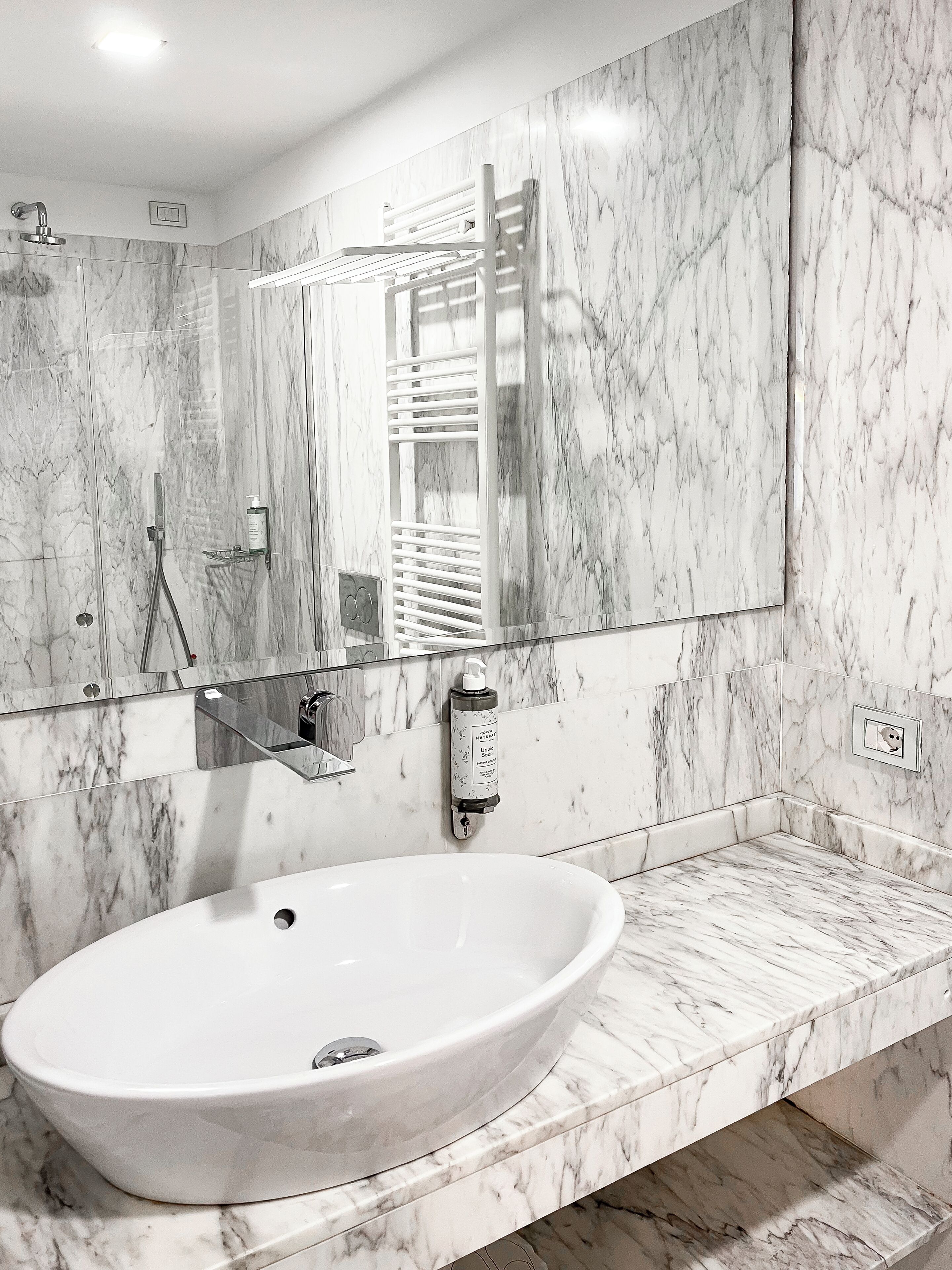Une salle de bain dotée d’un grand lavabo ovale, d’une douche en verre et d’un pare-baignoire en marbre.