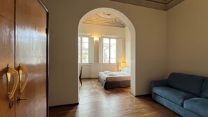 A hotel room with a wooden wardrobe, a blue sofa, a bed with a white duvet, and a wooden floor. - Hotel la Scala (Florence)