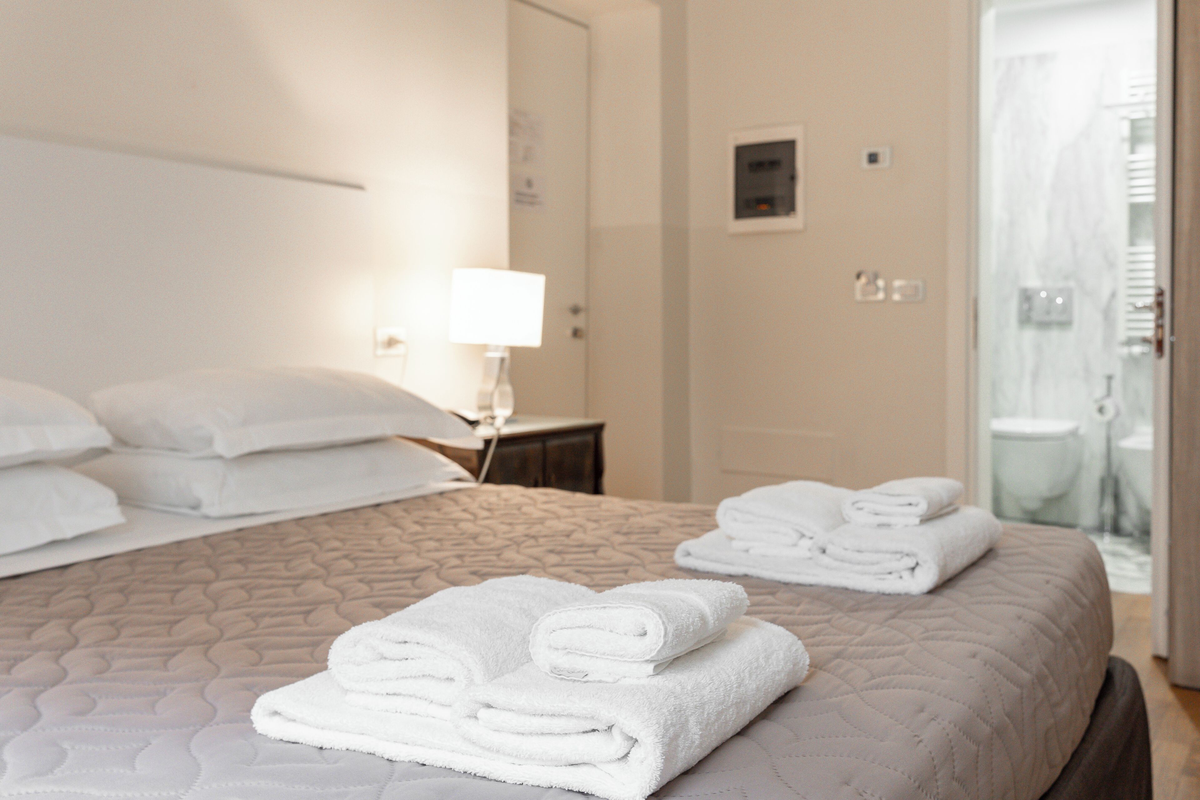 A hotel room with a neatly made bed, a bedside lamp, and a bathroom visible through an open door.