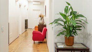A hallway with a wooden floor, a red chair, a potted plant, and a small table. - Hotel la Scala (Florence)