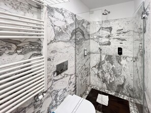 A bathroom with marble walls, a glass shower enclosure, and a white towel on the floor. - Hotel la Scala (Florence)